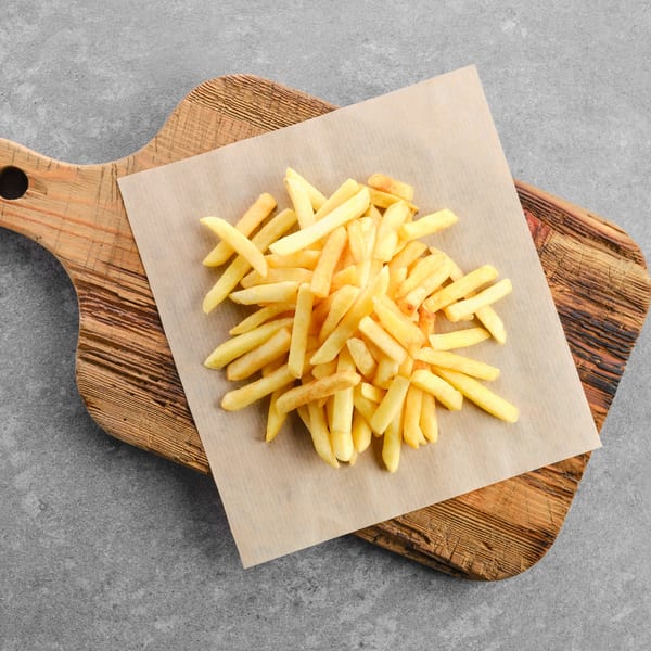 Golden french fries piled on parchment paper, served on a rustic wooden cutting board.