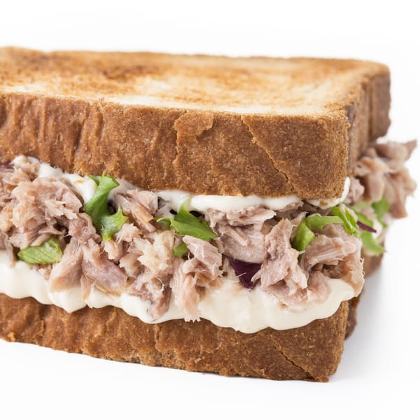 A close-up of a tuna salad sandwich on toasted bread with lettuce and mayonnaise.