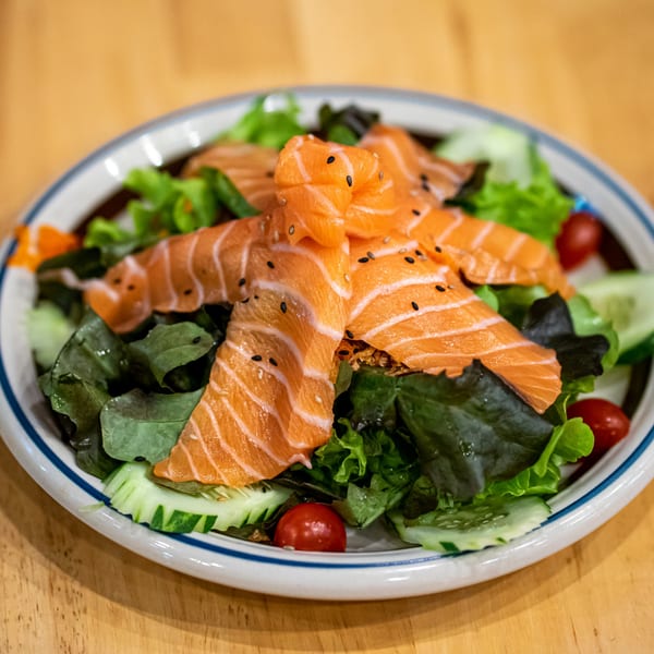 Fresh salmon sashimi salad with mixed greens, cucumber, cherry tomatoes, and sesame seeds.